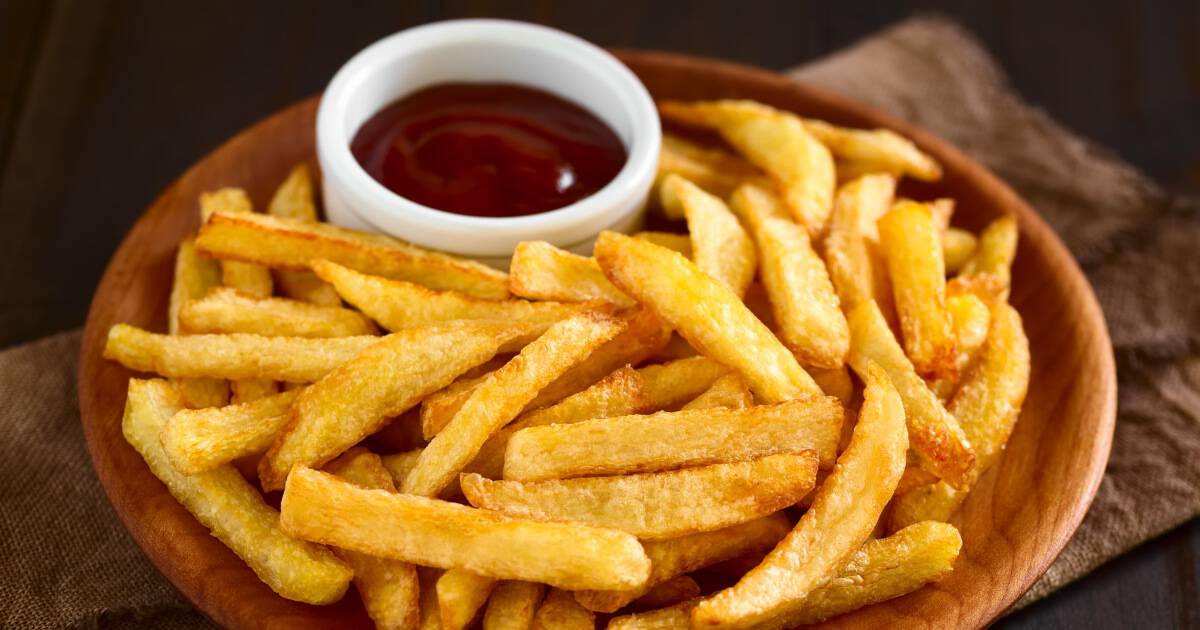 Plate covered in French fries and a small cup of ketchup