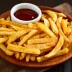Plate covered in french fries and a small cup of ketchup