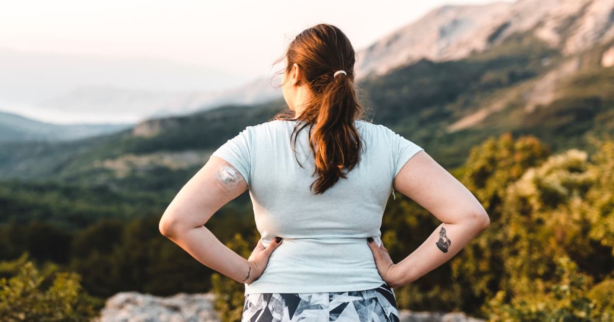 Woman wearing a CGM device near a ledge and looks out at the sunset.