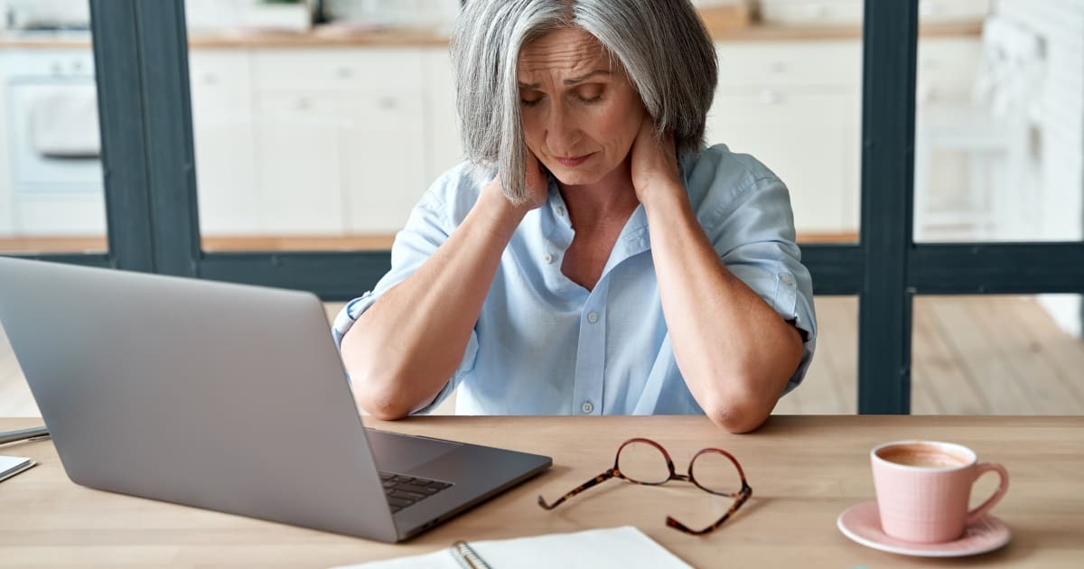 Woman in front of laptop holds her head in her hands.