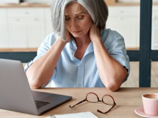 Woman in front of laptop holds her head in her hands.