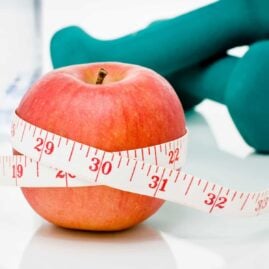 Measuring tape wrapped around a red apple with weights in the background