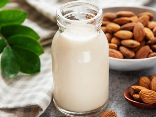 Glass of almond milk next to a dish of almonds