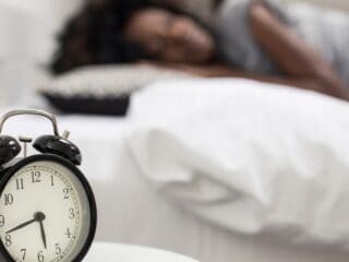 Close-up photo of an alarm clock and a woman sleeping in the background.