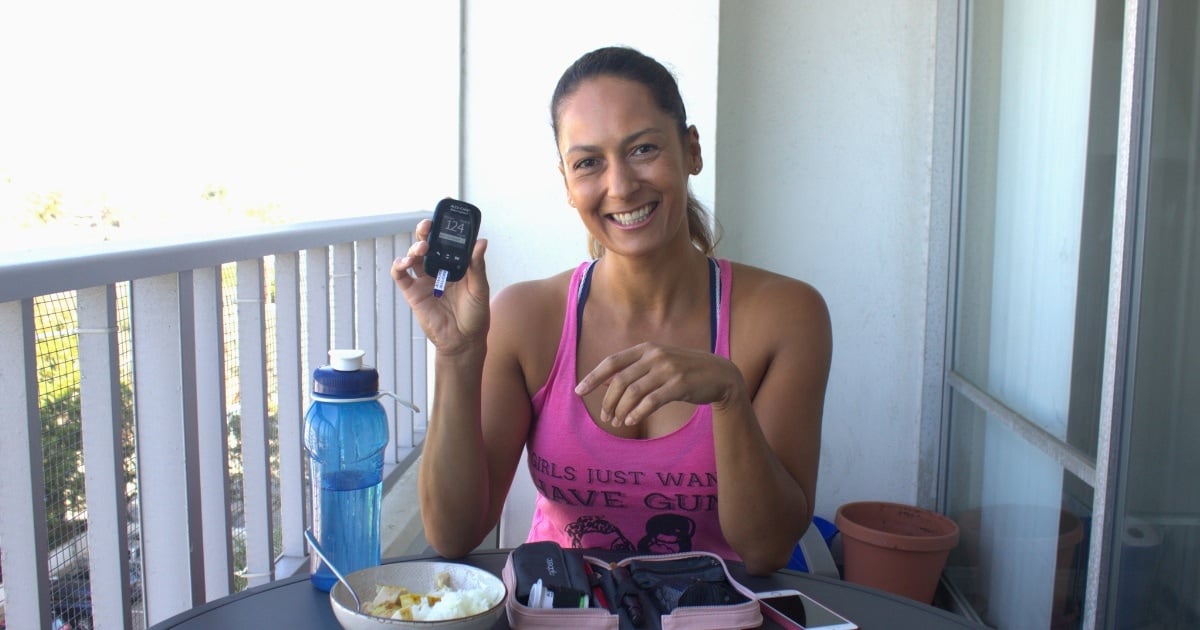 Christel holding a blood sugar meter while eating lunch on the balcony