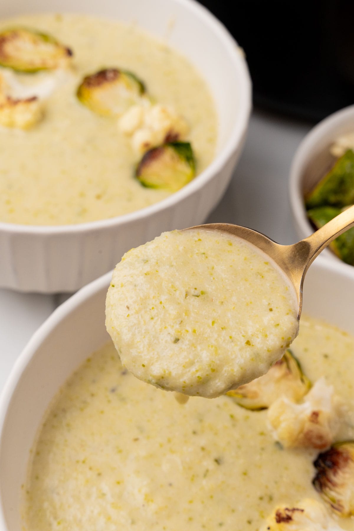 Spoonful of Creamy Cauliflower Soup with Brussels Sprouts held over pot of soup