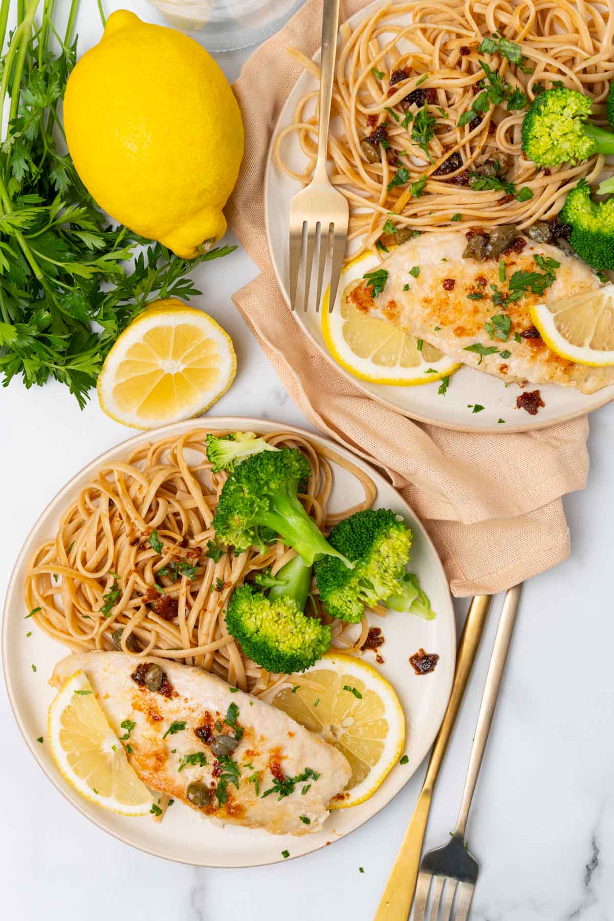 Two plates of chicken scallopini on a table with lemons