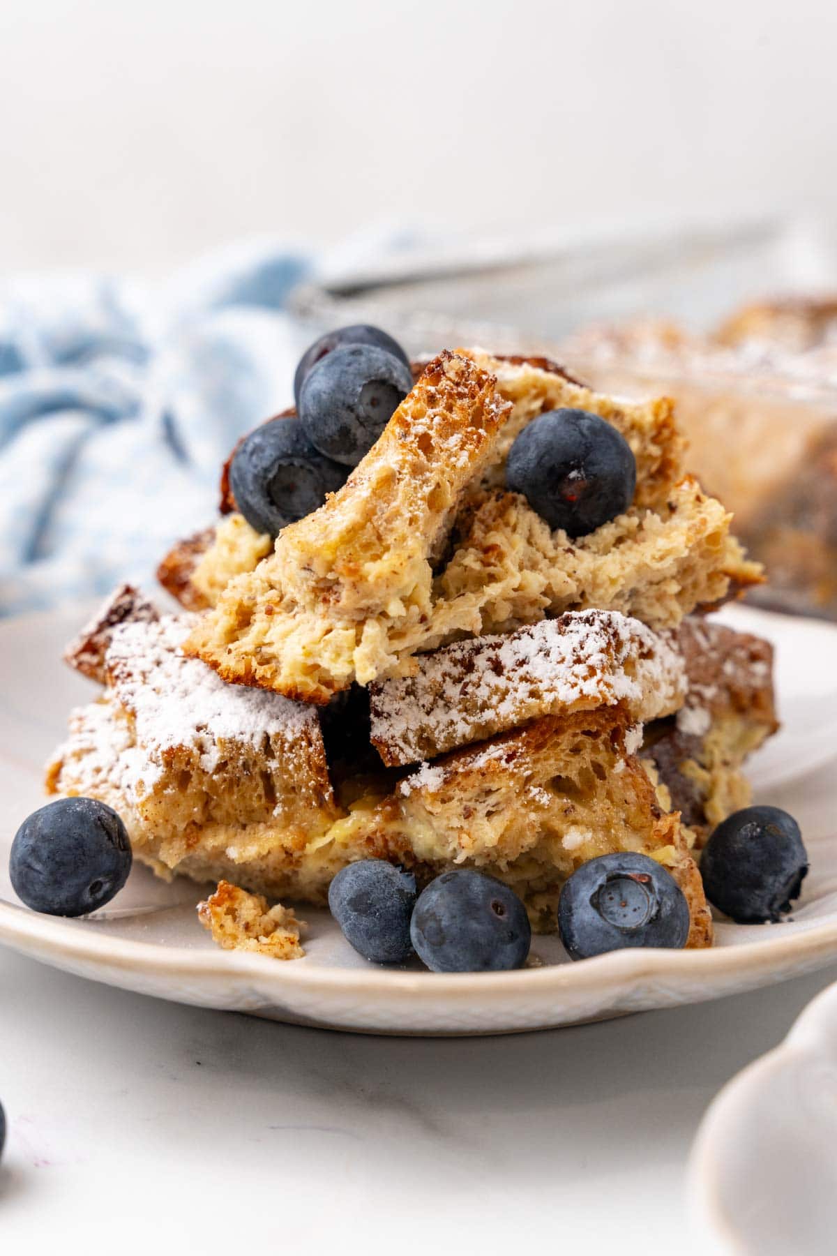 Close-up of low-carb bread pudding with blueberries on a white plate sitting on top of a white counter