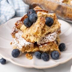 Closeup of low-carb bread pudding on a white scalloped plate topped with fresh blueberries